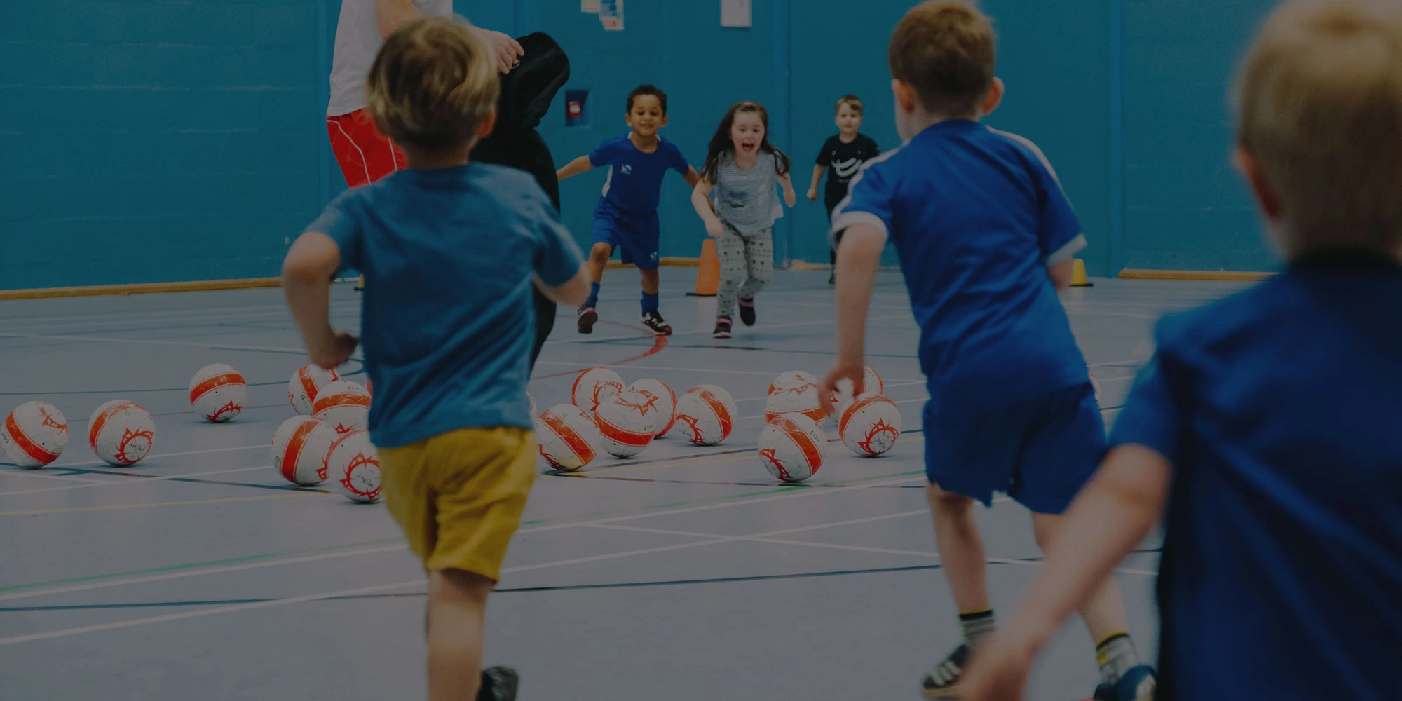 Children running towards footballs at a Kick-A-Bout class